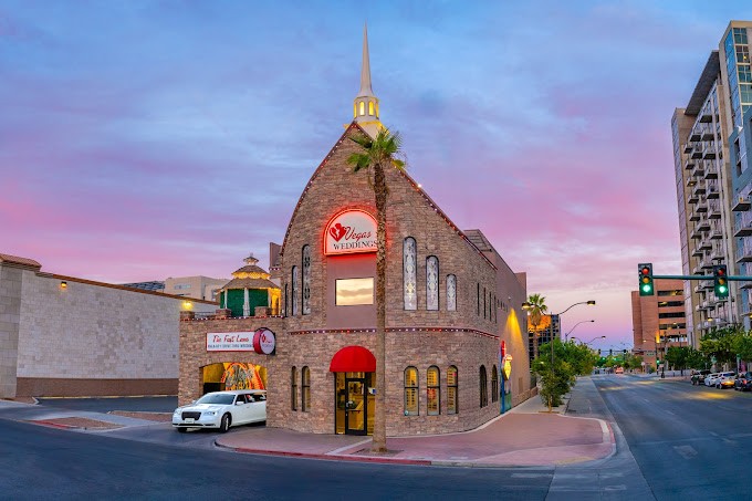 The Vegas Weddings chapel at dusk, with a brick front, steeple and red neon sign